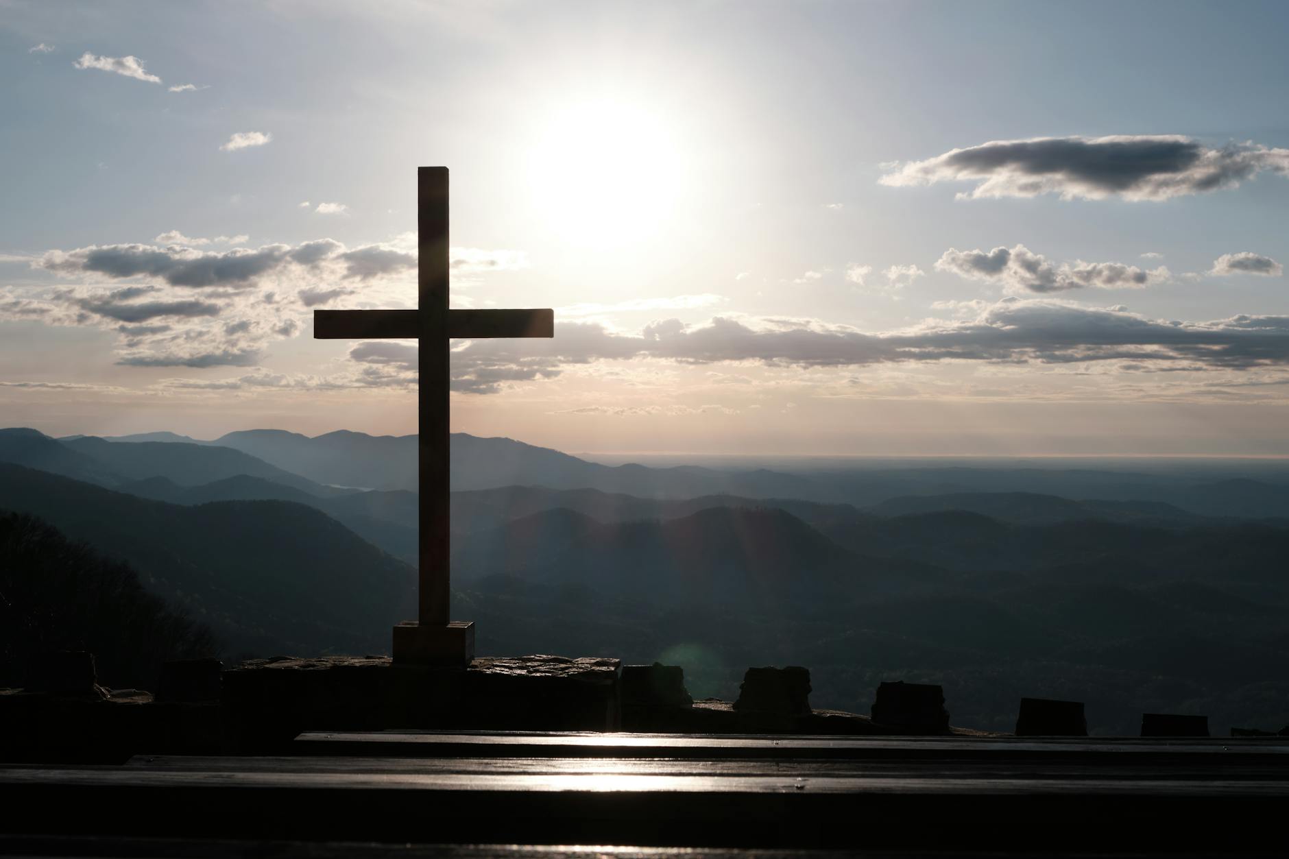 Wooden cross silhouetted against a sunset over mountain ranges